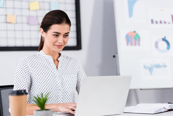 happy businesswoman looking at laptop on desk with blurred foreground - Photo, Image