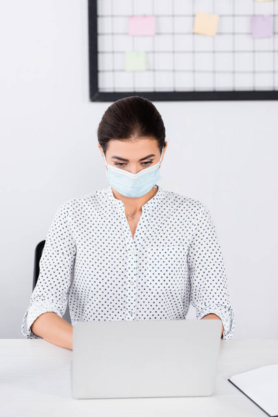 businesswoman in medical mask using laptop in office - Foto, afbeelding