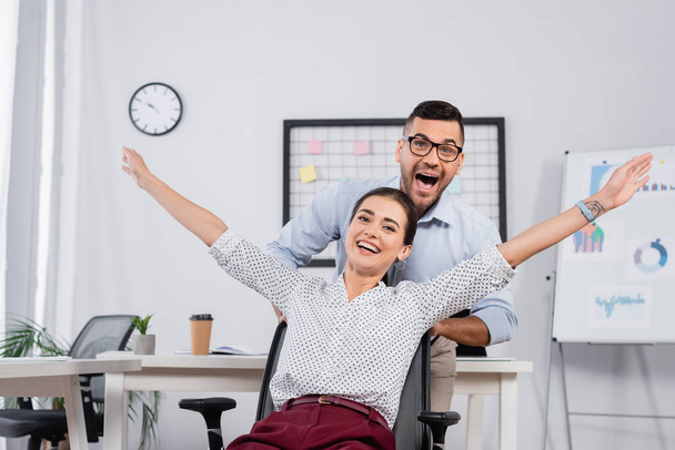 excited businessman behind amazed businesswoman with outstretched hands on chair - Фото, зображення