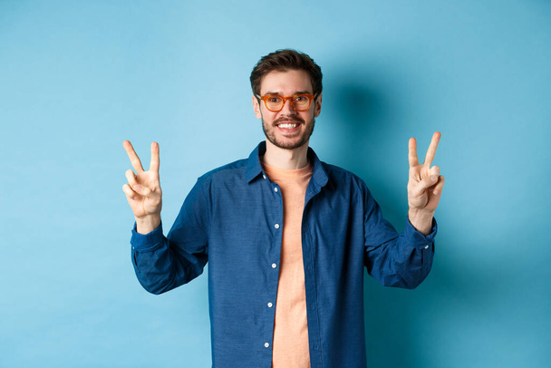 Χαρούμενος τύπος ποζάρουν με την ένδειξη ειρήνης σε νέα γυαλιά, έννοια της προώθησης κατάστημα γυαλιών - Φωτογραφία, εικόνα