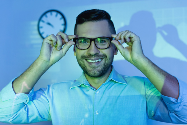 happy businessman adjusting glasses and smiling in office - Photo, Image