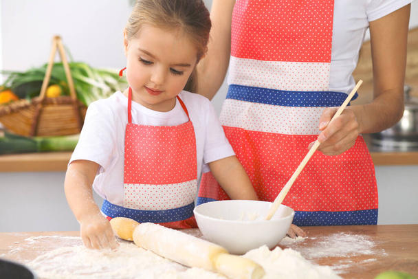 Mother and her cute daughter prepares the dough at wooden table. Homemade pastry for bread or pizza. Bakery background - Foto, Bild
