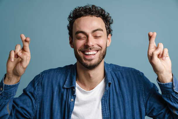 Happy handsome guy laughing while looking fingers crossed isolated over blue background - Foto, Bild