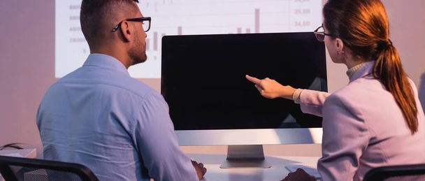 businesswoman in glasses pointing with finger at computer monitor with blank screen near coworker in office, banner - Фото, изображение