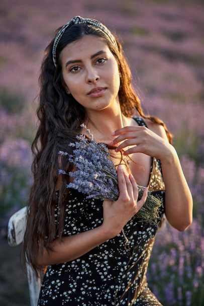 Фото кавказской молодой женщины в платье, держащей букет цветов, летом на открытом через лавандовое поле - Фото, изображение