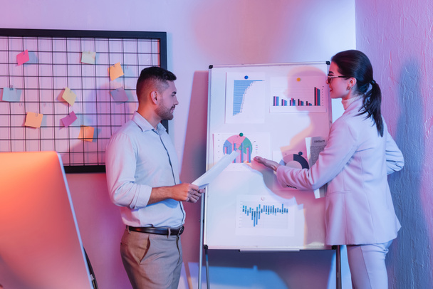 businessman looking at businesswoman pointing with hand at flipchart with charts and graphs - Foto, Bild