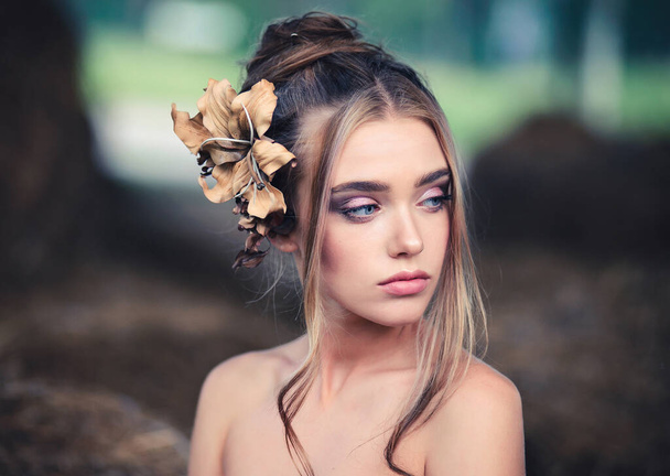 A beautiful young woman with healthy clear skin and beige flower in her hairstyle. Outdoor beauty portrait - Fotó, kép