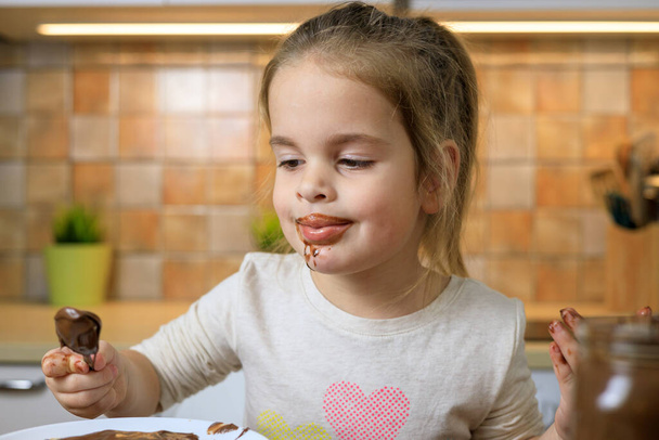 Kislány eszik csokoládé krémet kanállal - Fotó, kép