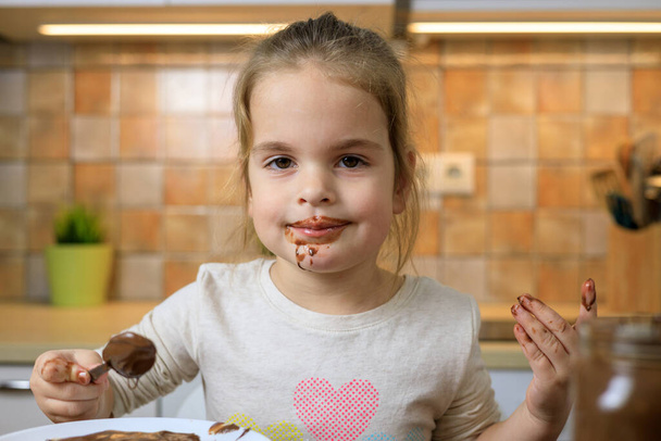 Kislány eszik csokoládé krémet kanállal - Fotó, kép