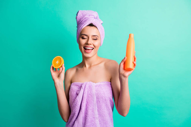 Photo of young girl hold orange shampoo bottle wear violet towel turban isolated teal color background - Foto, afbeelding