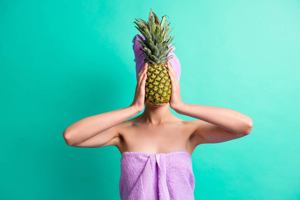 Photo of girl hands hold pineapple cover hide face wear purple towel turban isolated turquoise color background - Fotografie, Obrázek
