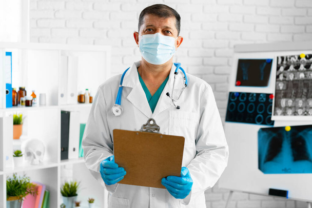 Middle aged doctor in mask holding cllipboard - Photo, image