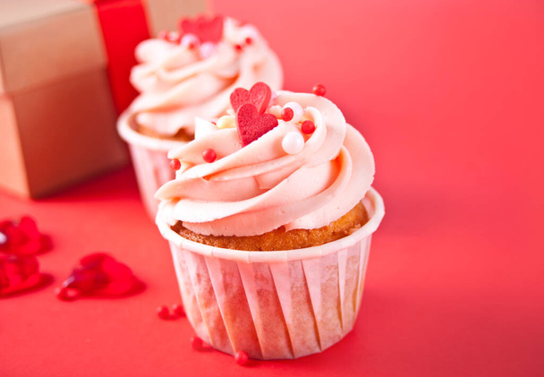 Valentines cupcakes cream cheese frosting decorated with heart candy and gift box on red background. - Фото, изображение