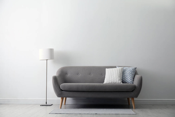 Graues Sofa mit Kissen nahe weißer Wand im stilvollen Wohnzimmerinterieur - Foto, Bild