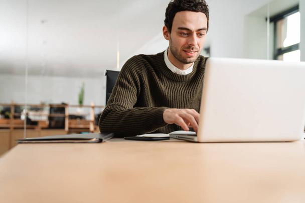 Lachende ondernemer werkt met een laptop en documenten in een kantoor - Foto, afbeelding