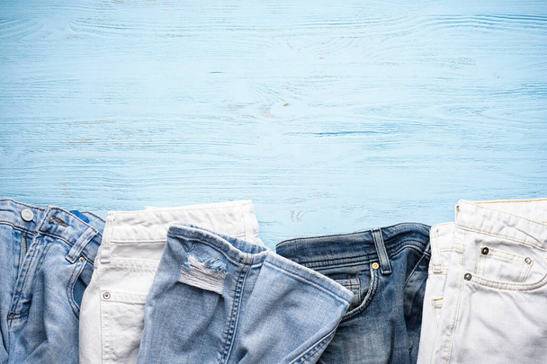 青い木製の背景に別のジーンズのズボン、トップビュー。テキストのスペース. - 写真・画像
