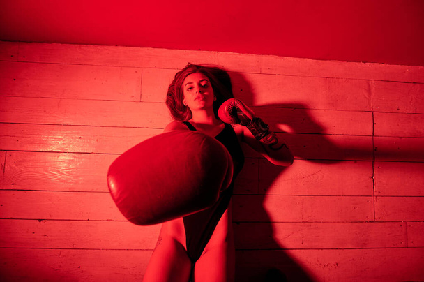 Bella donna con i guanti da boxe rossi sdraiata sul pavimento della palestra. Forza e motivazione. Boxe e stile fitness. - Foto, immagini