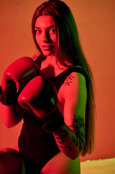 Beautiful woman with the red boxing gloves looking back and sitting on the floor. Strength and motivation. Boxing and fitness style. - Fotó, kép