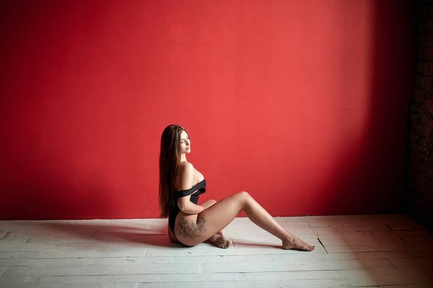 Portrait of a tattoo woman wearing in a black bodysuit sitting on the studio floor. Fashion concept - Фото, зображення