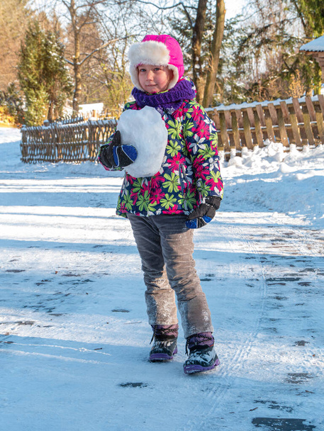 Мила дитина в зимовому одязі грає зі снігом на природі. Сімейний активний відпочинок на гірськолижному курорті. Зимові канікули. Маленька смішна дівчинка мандрівник посміхається сміється весело кидаючи сніжки
 - Фото, зображення