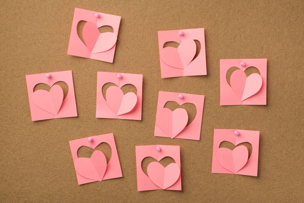 Gelukkig Valentijnsdag concept. Foto van pastelroze stickers met geslepen hartjes bevestigd aan het houten bord met spelden - Foto, afbeelding