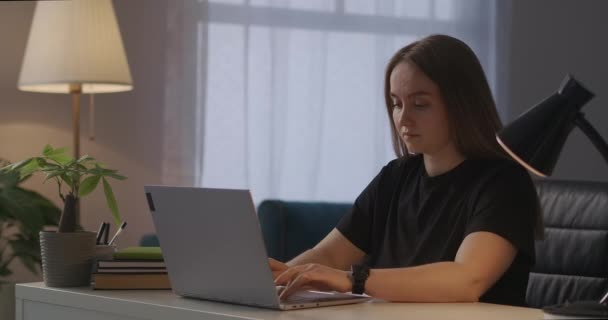 mujer agotada con el ordenador portátil en la oficina en casa en el momento de la noche, escribiendo en el teclado del ordenador portátil y sensación de dolor de cabeza - Metraje, vídeo