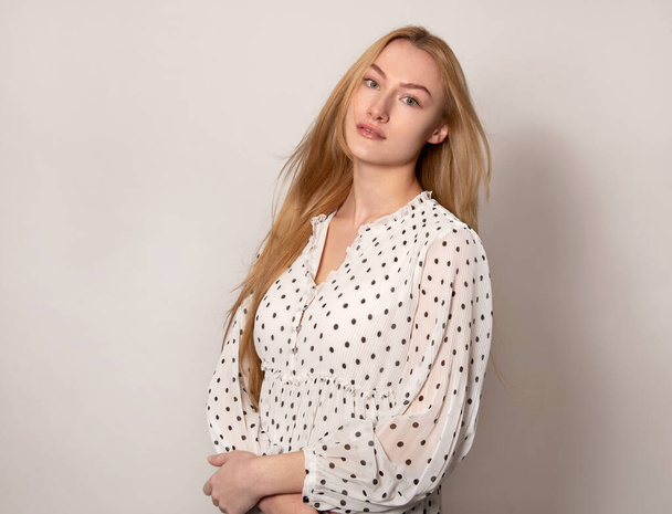 Beautiful young woman with blonde long shiny and healthy hair posing in dress on grey background - Foto, afbeelding