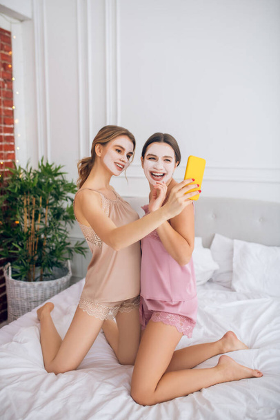 Two cute girls with facial masks making selfie - Фото, изображение