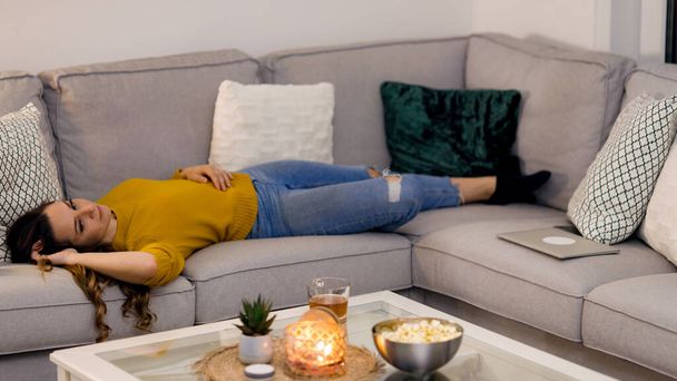 Young woman in her mid-20s lies on the couch - Photo, image