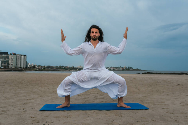 Stock photo of adult man with long hair doing yoga poses in the beach. - Foto, Imagem
