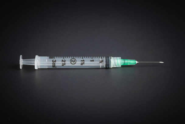 Um close-up com foco seletivo de uma seringa descartável para injetáveis de plástico higiênico de uso único em um fundo preto liso. - Foto, Imagem