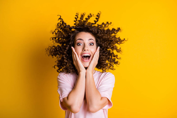 Photo portrait of amazed curly girl laughing touching cheeks with both hands opened mouth isolated on bright yellow color background - Photo, Image