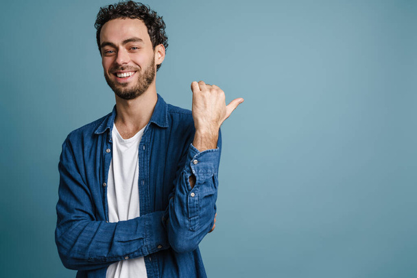Happy handsome guy smiling and pointing finger aside isolated over blue background - Foto, Imagem