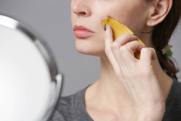 Mujer frotando cáscara de plátano en su cara para iluminar e hidratar la piel y reducir las arrugas. Cero residuos y concepto de cuidado natural de la piel. - Foto, Imagen