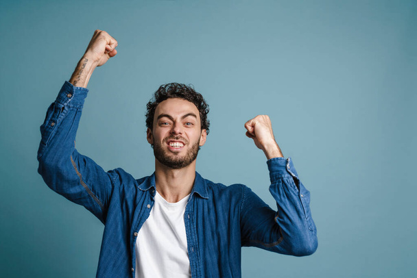 Happy young man celebrating success over blue background, looking at camera - Foto, afbeelding