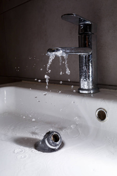 Gebrochener Wasserhahn im Waschbecken des Badezimmers. Spritzwasser aus dem silbernen Wasserhahn - Foto, Bild
