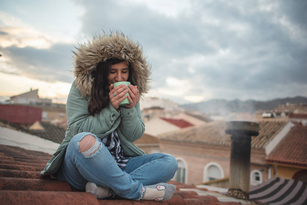 Жінка в момент розслаблення п'є чай на даху свого будинку
 - Фото, зображення