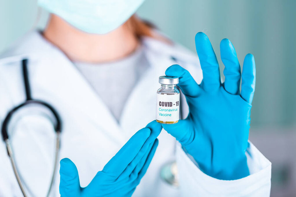 Mujer doctora o enfermera en uniforme y guantes con mascarilla protectora en laboratorio sosteniendo frasco de vacuna vial con COVID-19 Etiqueta de la vacuna contra el Coronovirus - Foto, Imagen