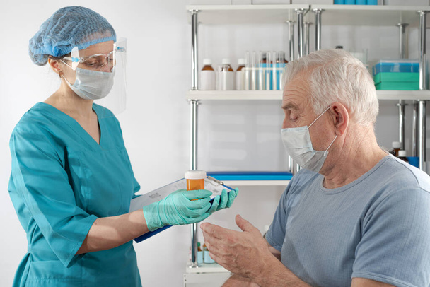 Female nurse holding a clipboard folder, giving prescription drug orange pill jar  to adult senior man. Doctor's appointment hospital healthcare case - Foto, Imagem
