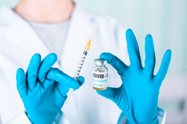 Woman doctor or nurse in uniform and gloves wearing face mask protective in lab holding medicine vial vaccine bottle with COVID-19 Coronovirus vaccine label - Φωτογραφία, εικόνα
