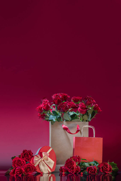 Grande saco de artesanato cheio de rosas; caixa de presente em forma de coração; rosas; contas em uma superfície de espelho. Dia dos Namorados ou convite romântico à noite. Encomenda e entrega de oficina de flores - Foto, Imagem