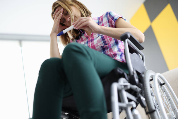 Tekerlekli sandalyedeki üzgün kadın hamilelik testine bakar. - Fotoğraf, Görsel