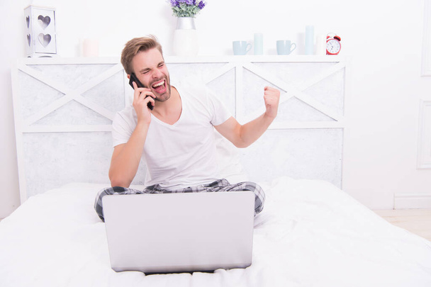 Its a deal. Happy man make winner gesture in bed. Phone conversation. Bet winner. Online betting - Фото, изображение
