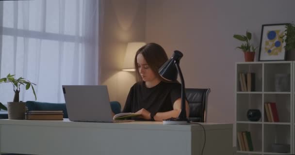 女性はノートパソコンの画面から情報を読みながら宿題を書いています - 映像、動画