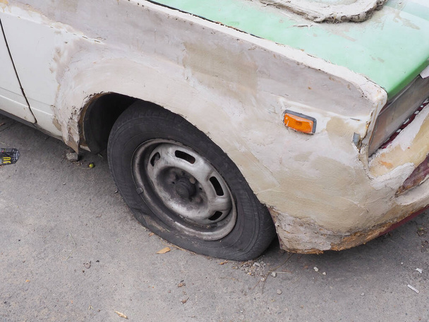 Fragmento de un coche viejo cubierto con masilla de textura gruesa blanca y con un neumático pinchado - Foto, imagen
