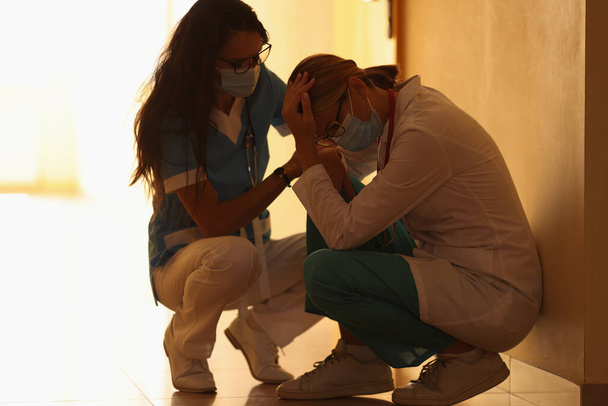 Két frusztrált orvos orvosi védőmaszkban ül a kórház folyosóján. - Fotó, kép