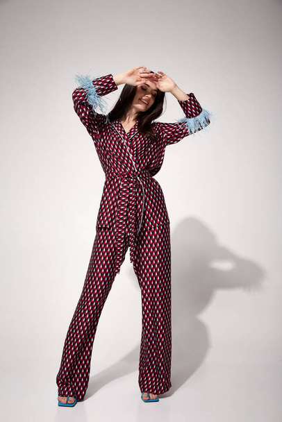 Pretty sexy woman beautiful face natural makeup brunette hair wear silk textile suit pants and blouse with feathers shoes comfort casual home dress luxury lifestyle pajama party glamour fashion model. - 写真・画像