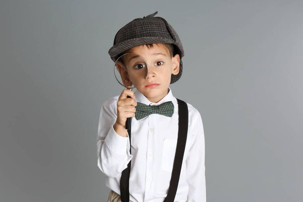 Little boy with magnifying glass playing detective on grey background - Photo, image
