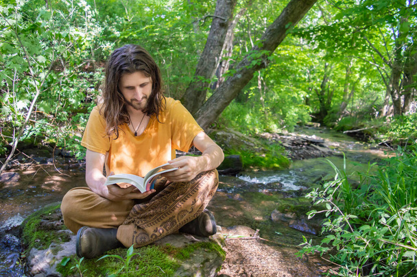 Νεαρός διαβάζει ένα βιβλίο στην όχθη ενός ποταμού. - Φωτογραφία, εικόνα
