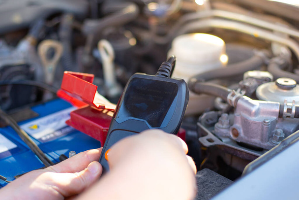 a car mechanic under the hood of a car diagnoses a car battery with a tester, close-up, repair and replacement of the battery - Photo, Image